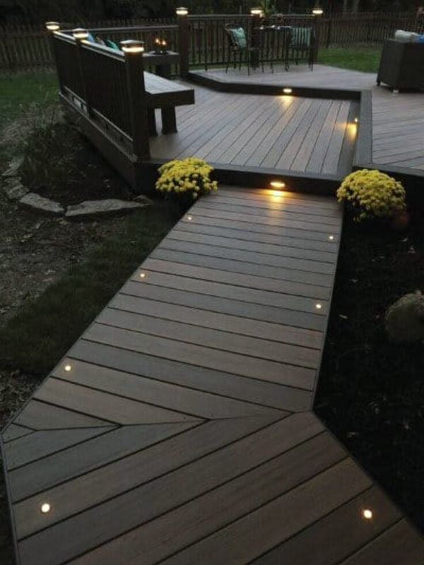 Example of a wooden boardwalk leading to custom deck with path lighting in a backyard.