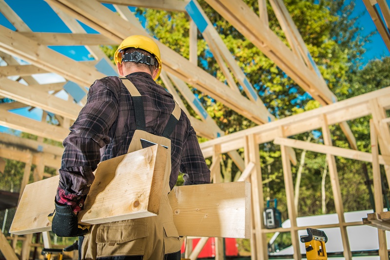 A carpenter carrying wood planks through a construction site